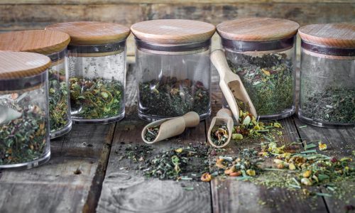 still life of loose tea in glass jar and wooden spoons on wooden background